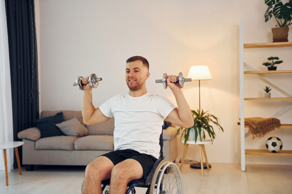 Man in a wheelchair doing a seated dumbbell shoulder press at home, showing exercise for people with disabilities